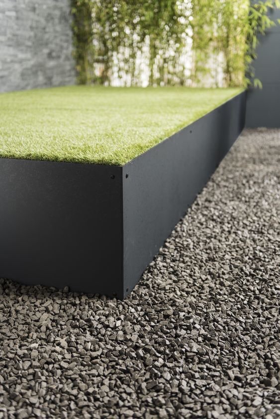 Eine Terrasse aus Schwarzstahl bildet den Rahmen für eine sauber verlegte Fläche aus Kunstrasen.