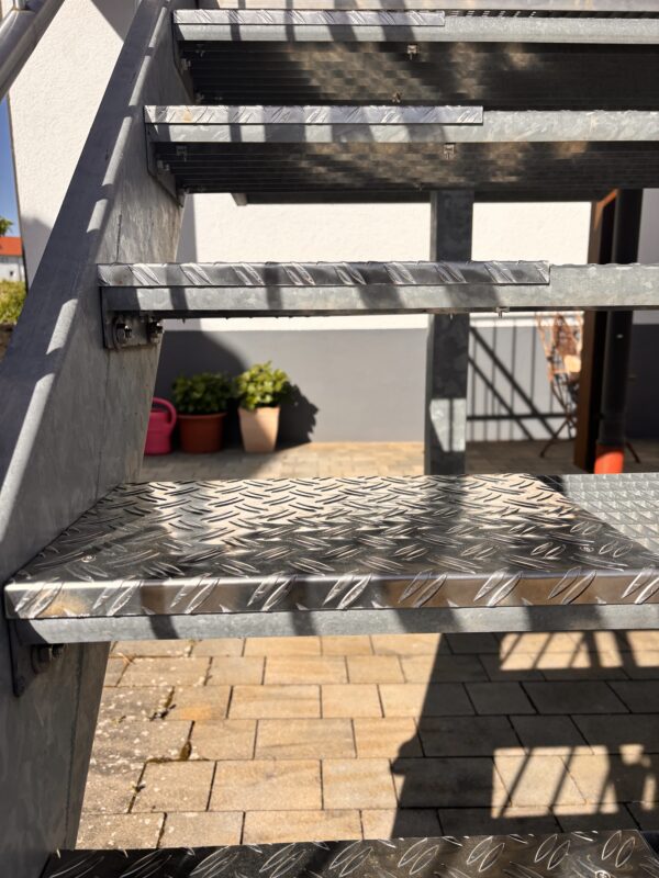 Seitliche Ansicht der Gittertreppe mit Aluminium-Riffelblech als geschlossene Trittfläche für Hundepfoten im Außenbereich.