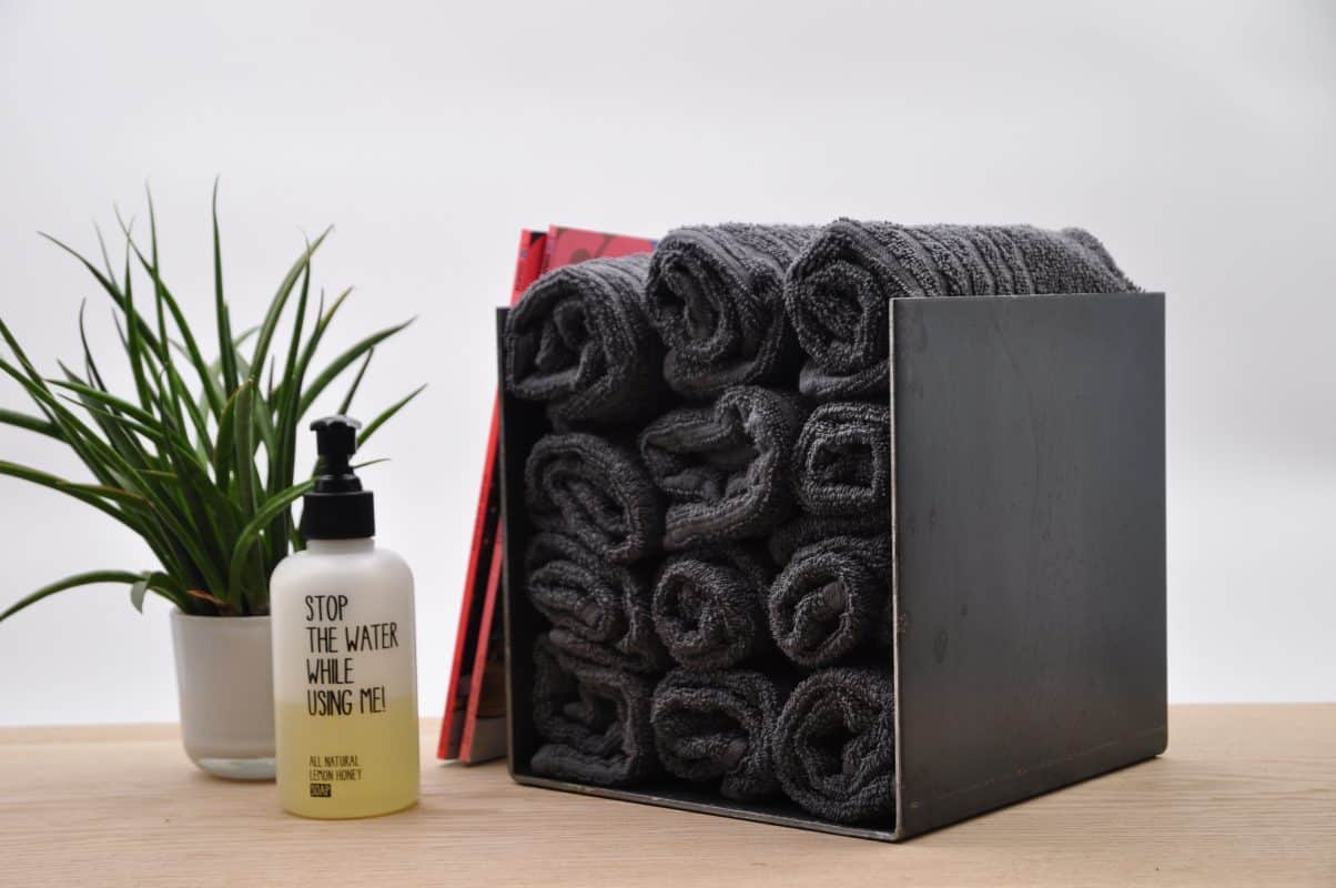 Schwarze Stahlbox mit gerollten Handtüchern auf Holzfläche.