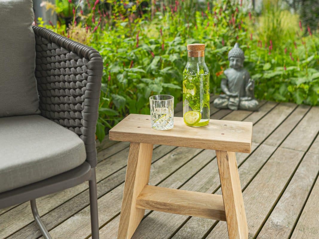 Kleiner Eichenholz-Hocker auf Terrasse mit Sommergetränk.