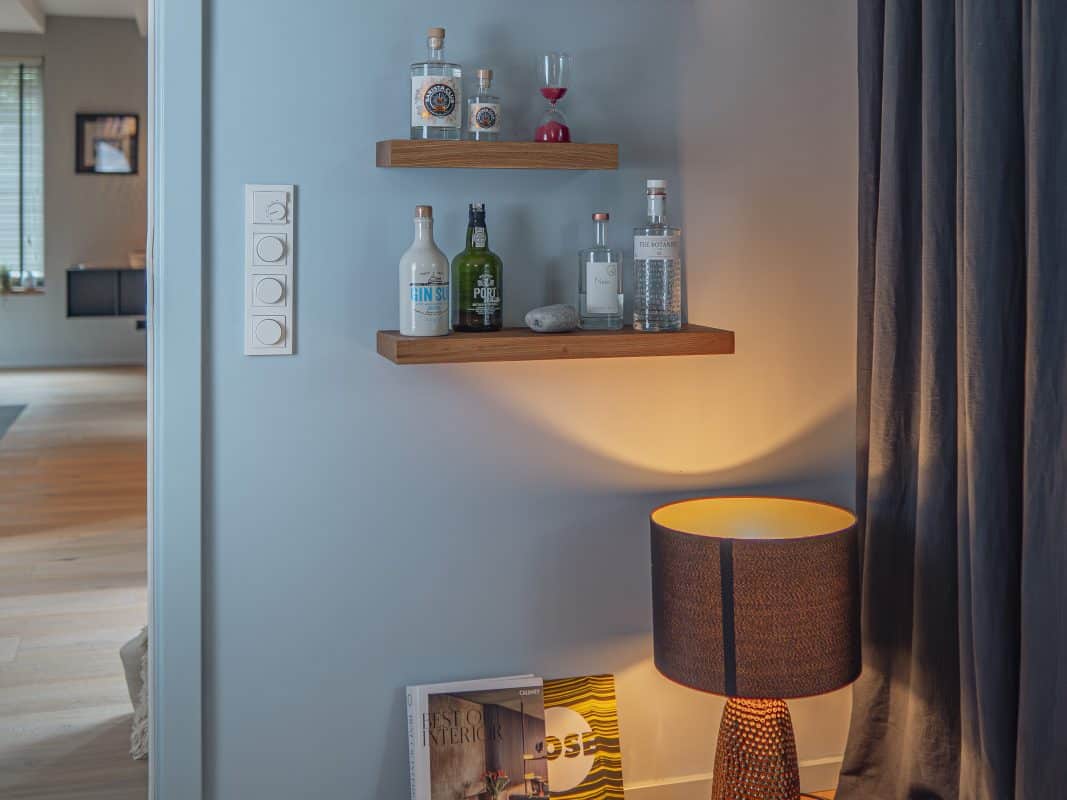Zwei schwebende Holzregale mit Spirituosenflaschen an blauer Wand.