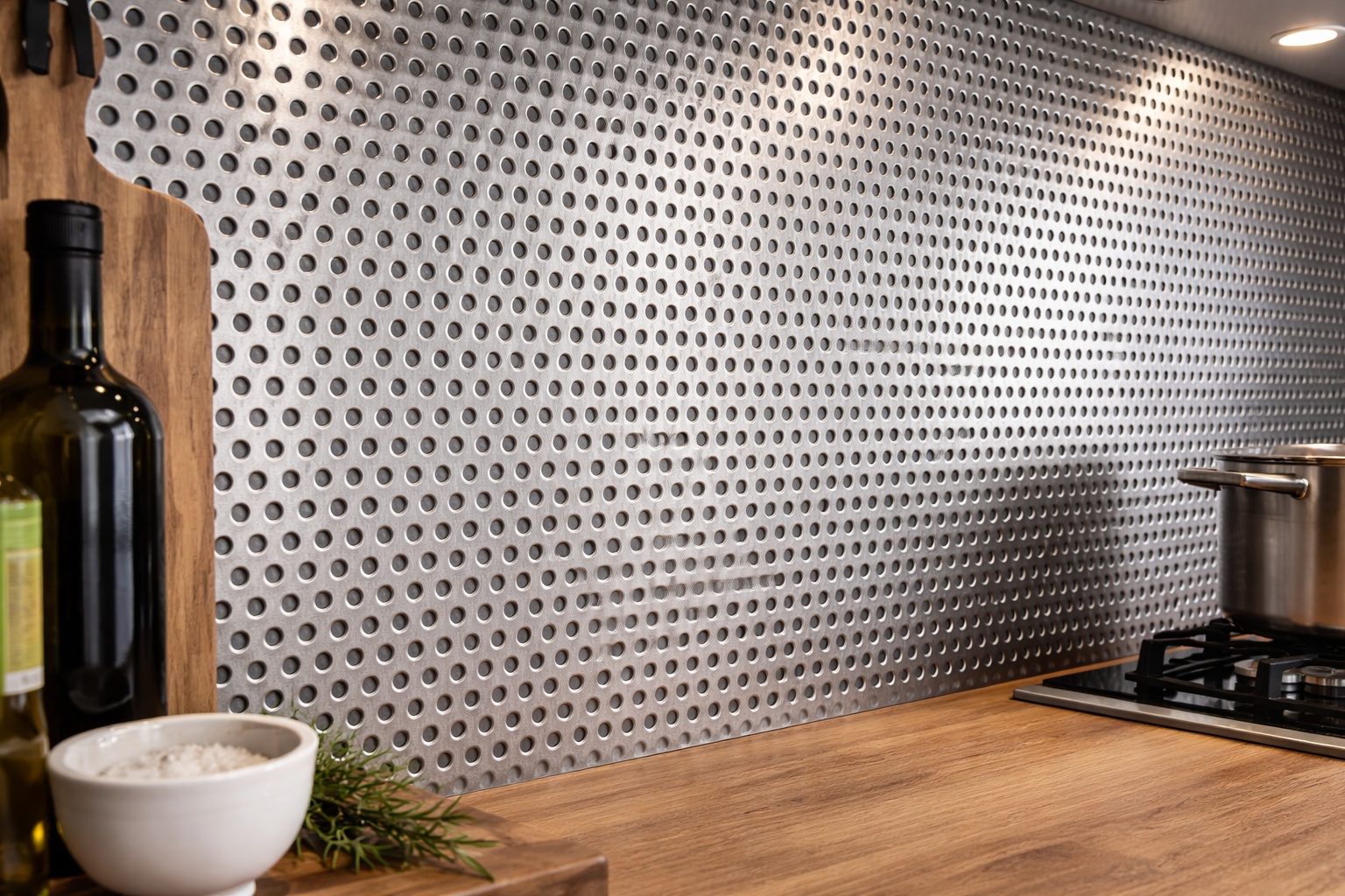 Eine Küchenrückwand aus rund gelochtem Edelstahl-Lochblech schützt den Kochbereich funktional.