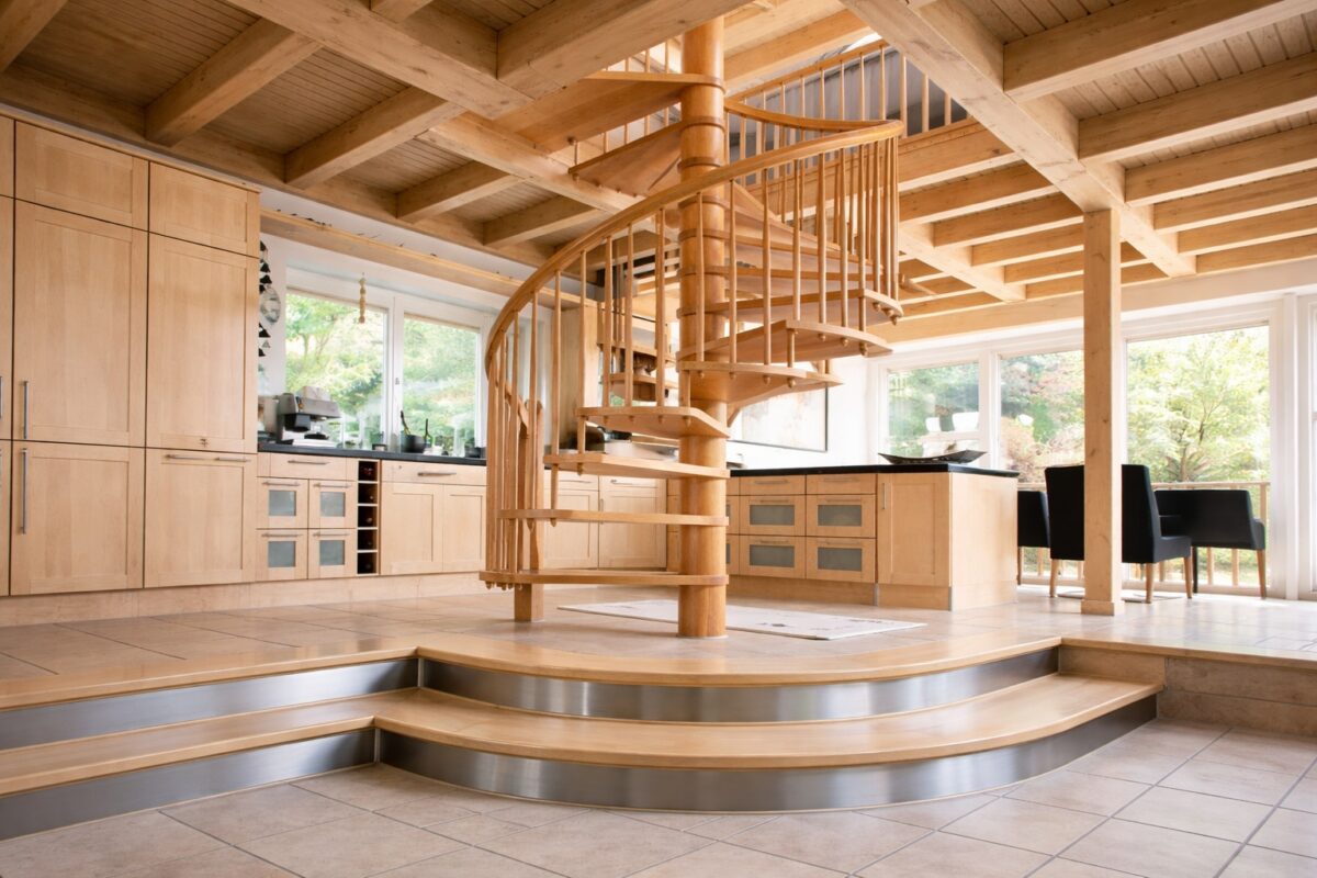 Hölzerne Wendeltreppe steht offen zwischen Küche, Essbereich und Holzdecke.