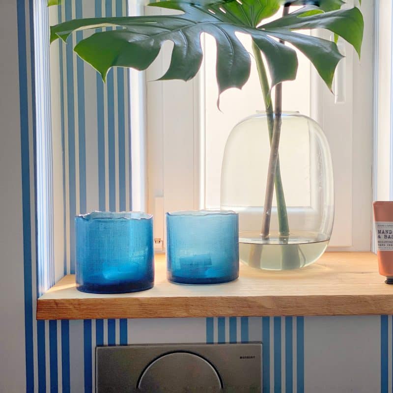 Holzfensterbank mit blauen Gläsern und Glasvase mit Monstera-Blatt.