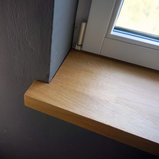 Fensterbank aus massiver Eiche, glatt geschliffen, mit natürlicher Maserung, montiert unter einem Fenster im Innenraum.