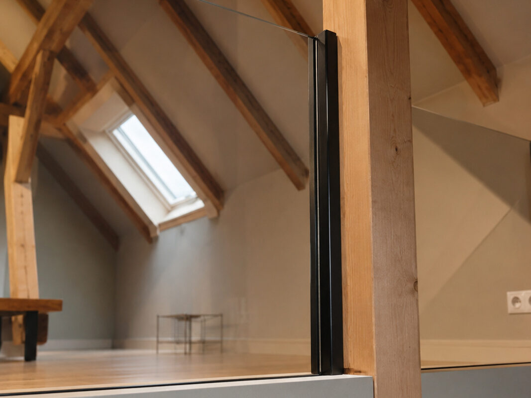 Nahaufnahme des VSG Glasgeländers mit schwarzer Glasklemme an der vorhandenen Holzkonstruktion der Galerie.