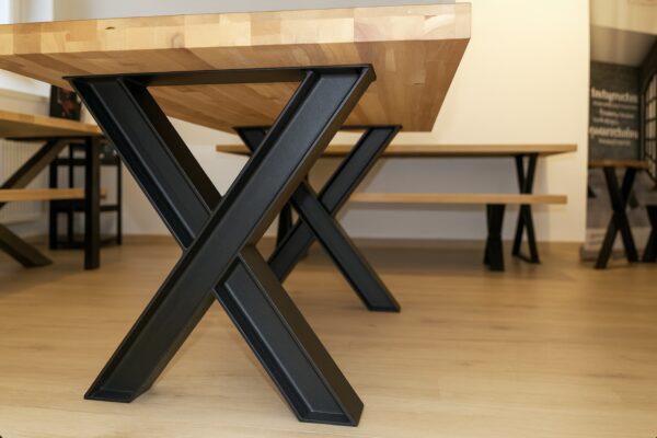 Der Holztisch steht auf schwarzen X-Gestellen aus robusten HEB-Stahlträgern im Showroom.
