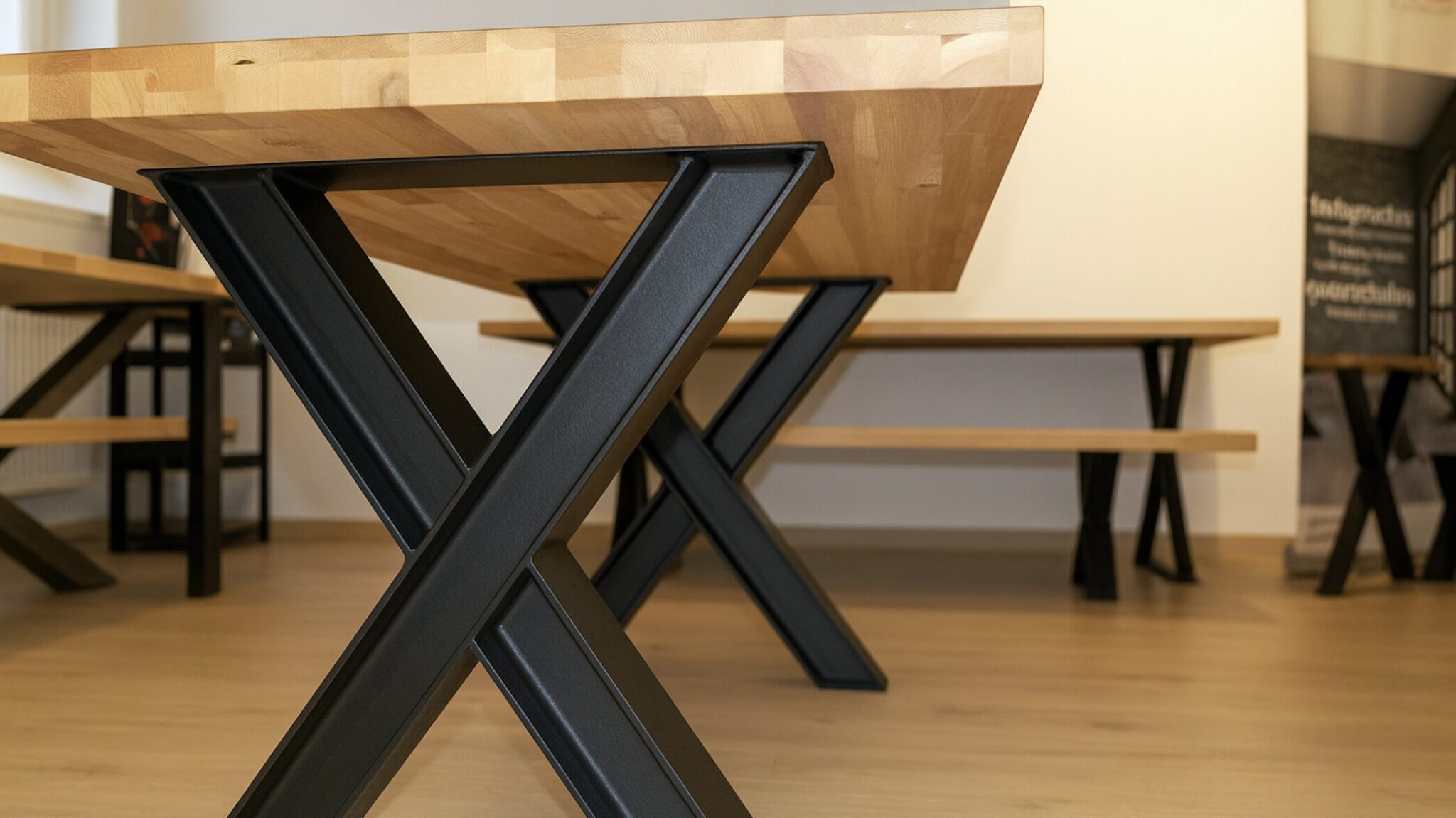 Ein Holztisch steht auf schwarzen X-Gestellen aus robusten HEB-Stahlträgern in einem Raum.
