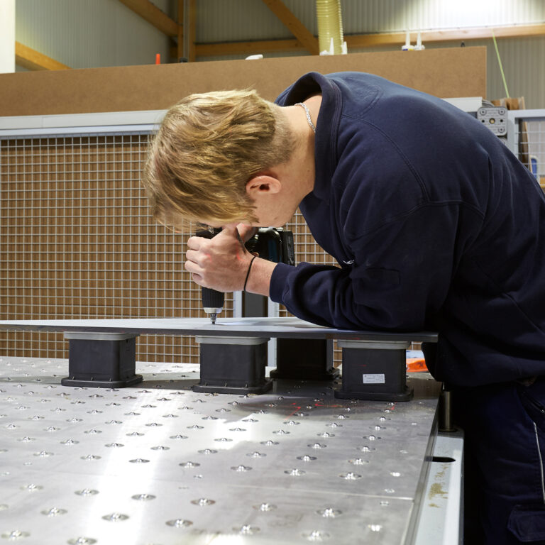 Ein Mitarbeiter bearbeitet ein Werkstück an einer Maschine in einer Werkstatt.
