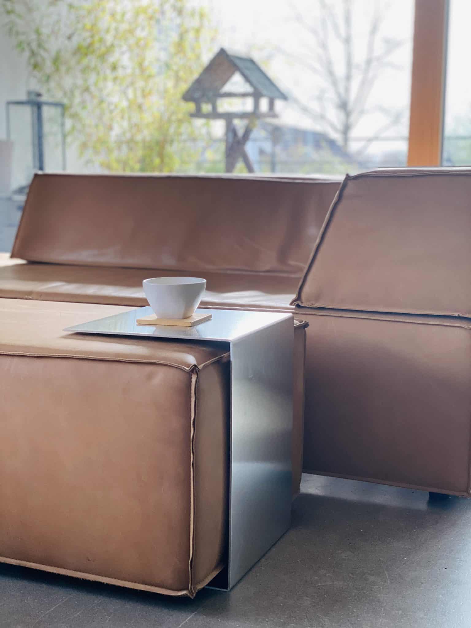 Ein braunes Ledersofa wird von einem modernen Metall-Beistelltisch mit einer Kaffeetasse ergänzt.