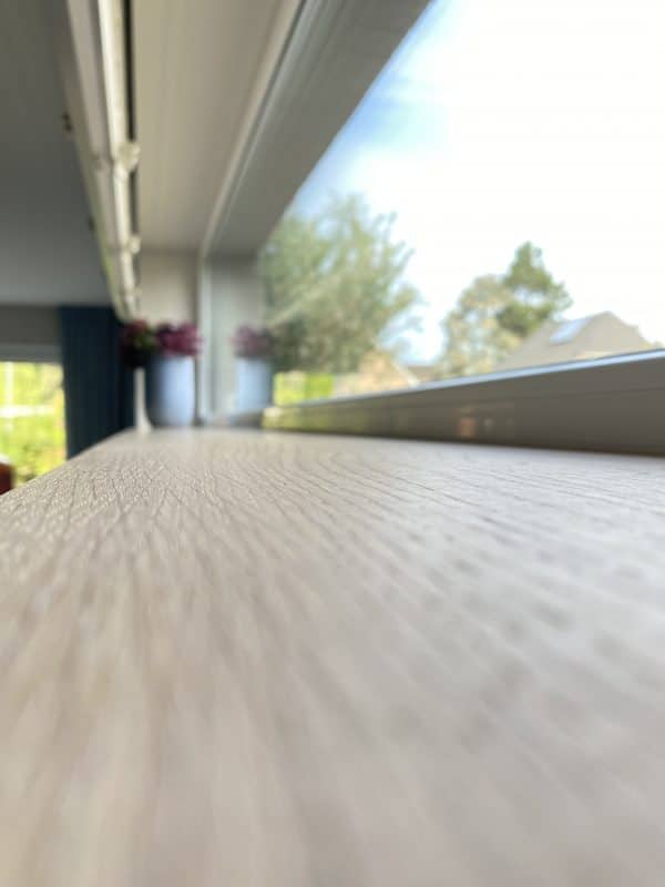 Nahaufnahme einer hellen Holzfensterbank mit einer Vase und Blick nach draußen.