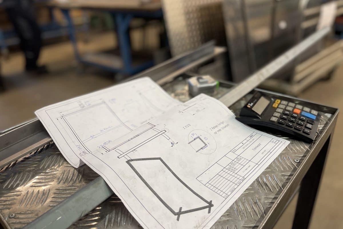 Technische Zeichnung und Taschenrechner auf Werkbank mit Riffelblech.