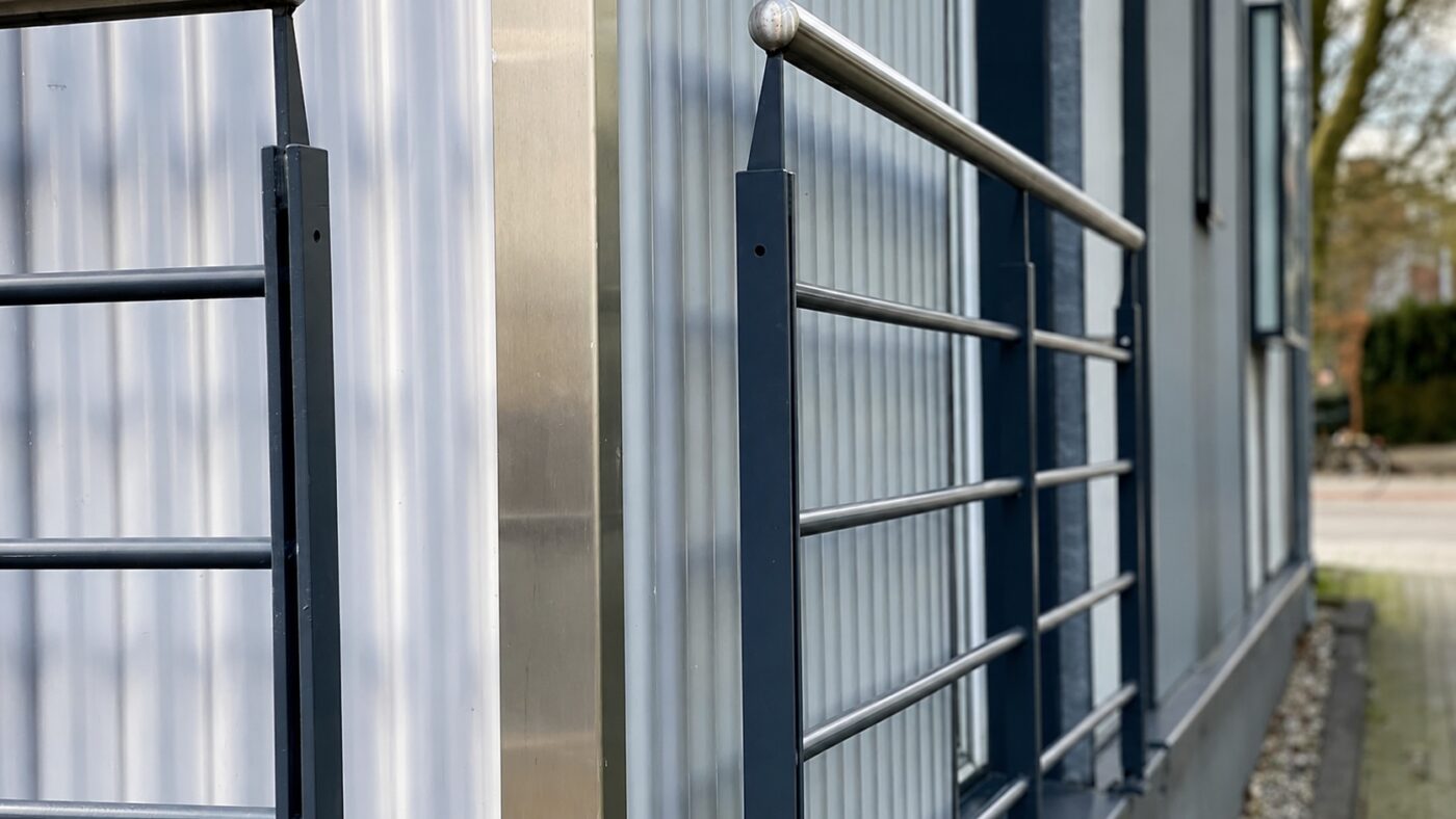 Ein Edelstahlgeländer verläuft entlang einer modernen Fassade mit Glasprofilen.