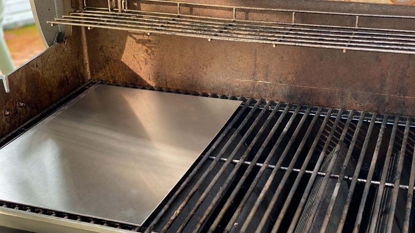 Eine Edelstahl-Grillplatte liegt auf einem Grillrost in einem geöffneten Grill.