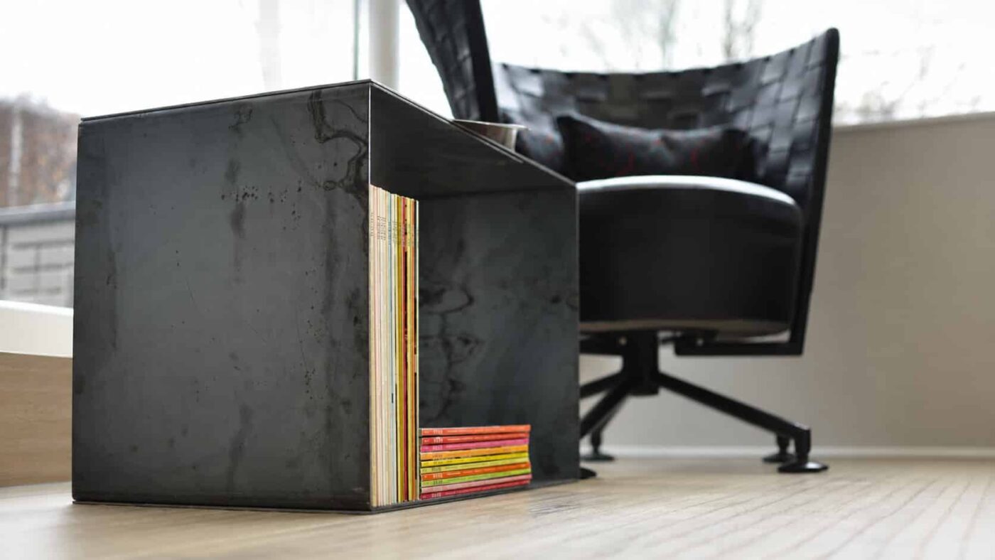 Ein schwarzes Stahlregal mit Büchern steht in einem hellen Wohnraum.