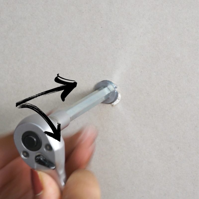 Nahaufnahme eines Metall-Hohlraumdübels mit Schraube, bereit zur Montage in einer Gipskartonwand.​