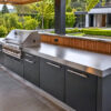 Luxuriöse Outdoor Küche mit Edelstahl Arbeitsplatte, Grill und anthrazitfarbenen Fronten im Garten.