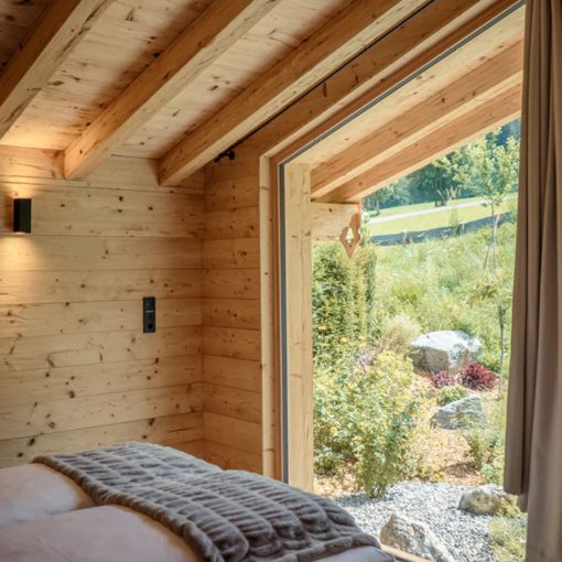 Modernes Tiny House mit großen Fenstern und Blick in den Garten, kompakte Wohnlösung mit naturnahem Wohnerlebnis. Titel:
