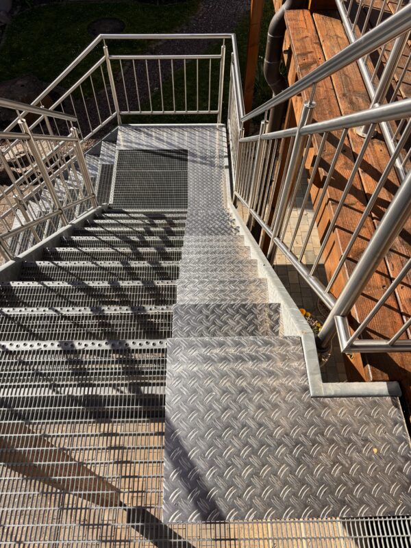 Stahltreppe mit geschlossener Laufspur aus Aluminium-Riffelblech neben offenen Gitterstufen für Hunde im Außenbereich.