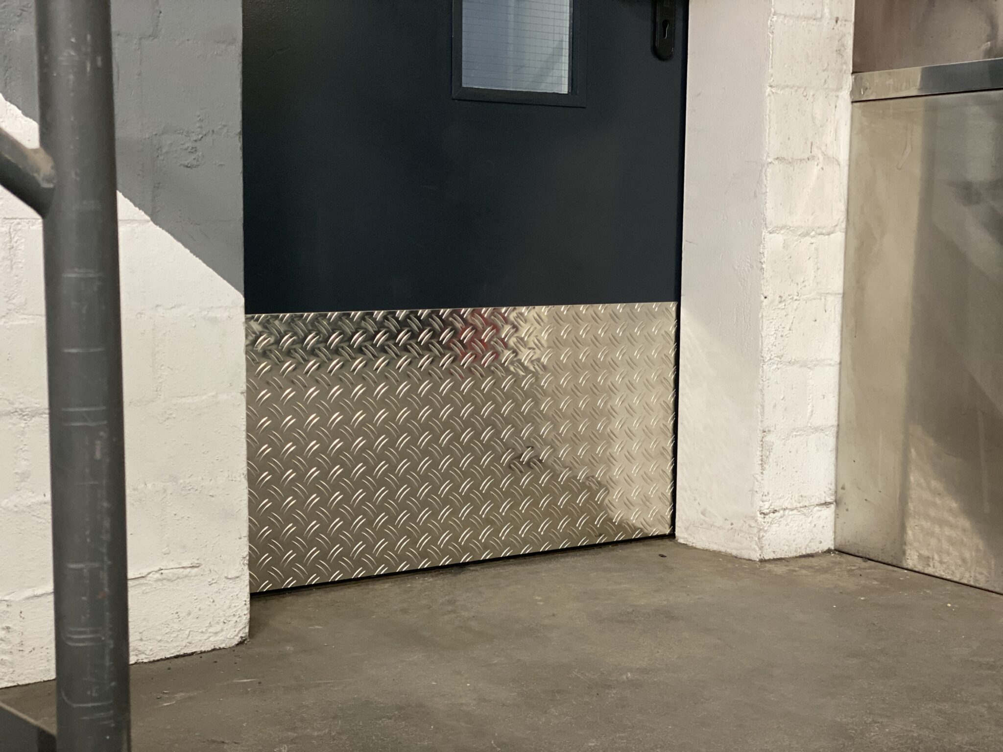 Ein Alu Riffelblech schützt eine Tür vor Beschädigungen.