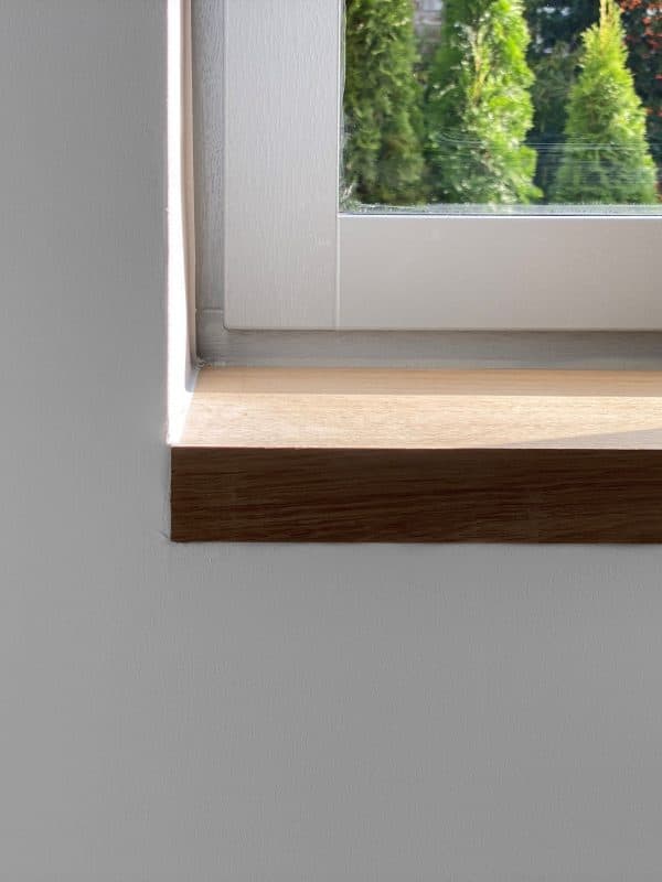 Nahaufnahme einer fertigen Holzfensterbank mit grüner Natur im Hintergrund.