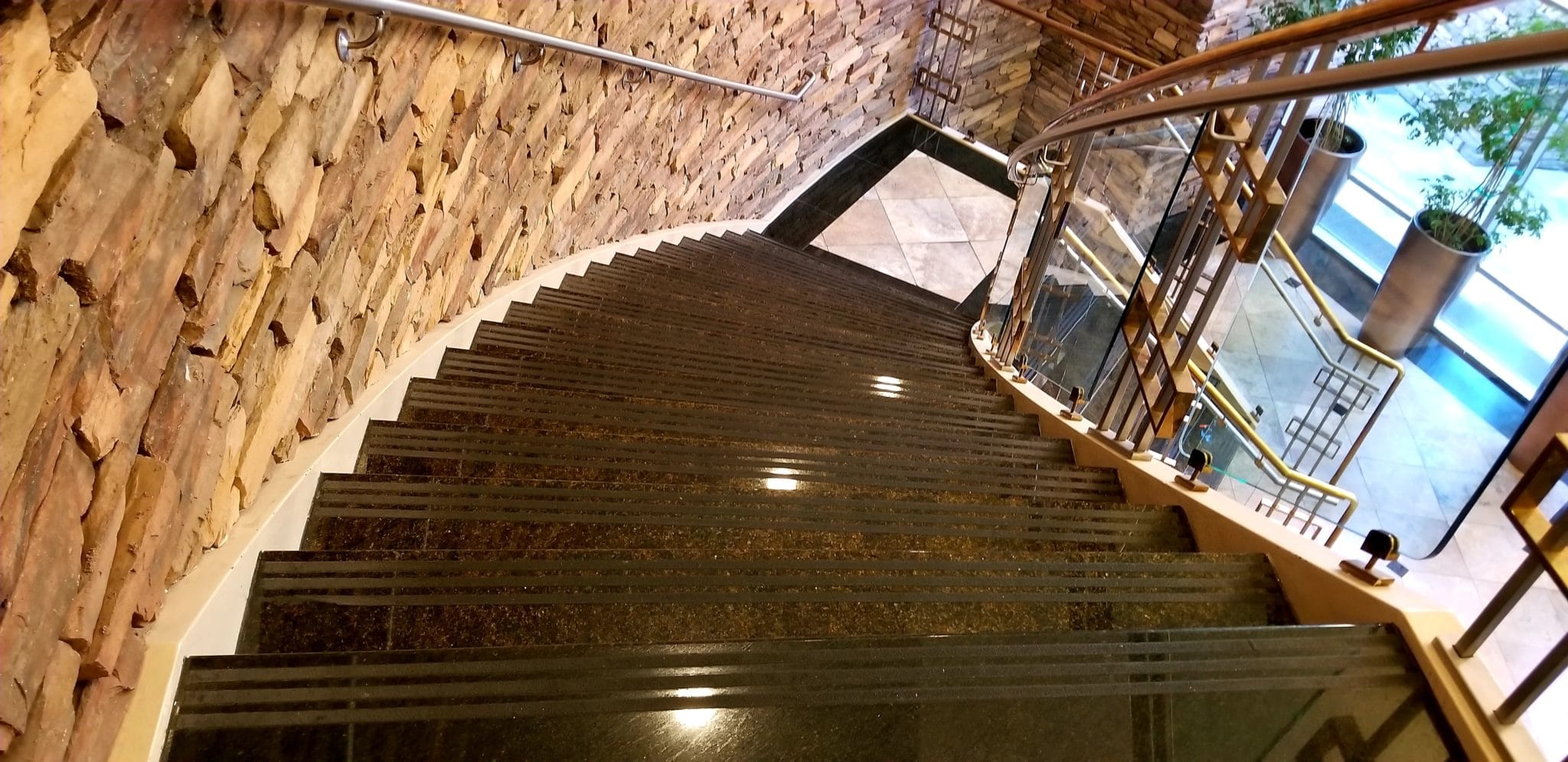 Geschwungene Treppe aus poliertem Naturstein mit Glasgeländer.