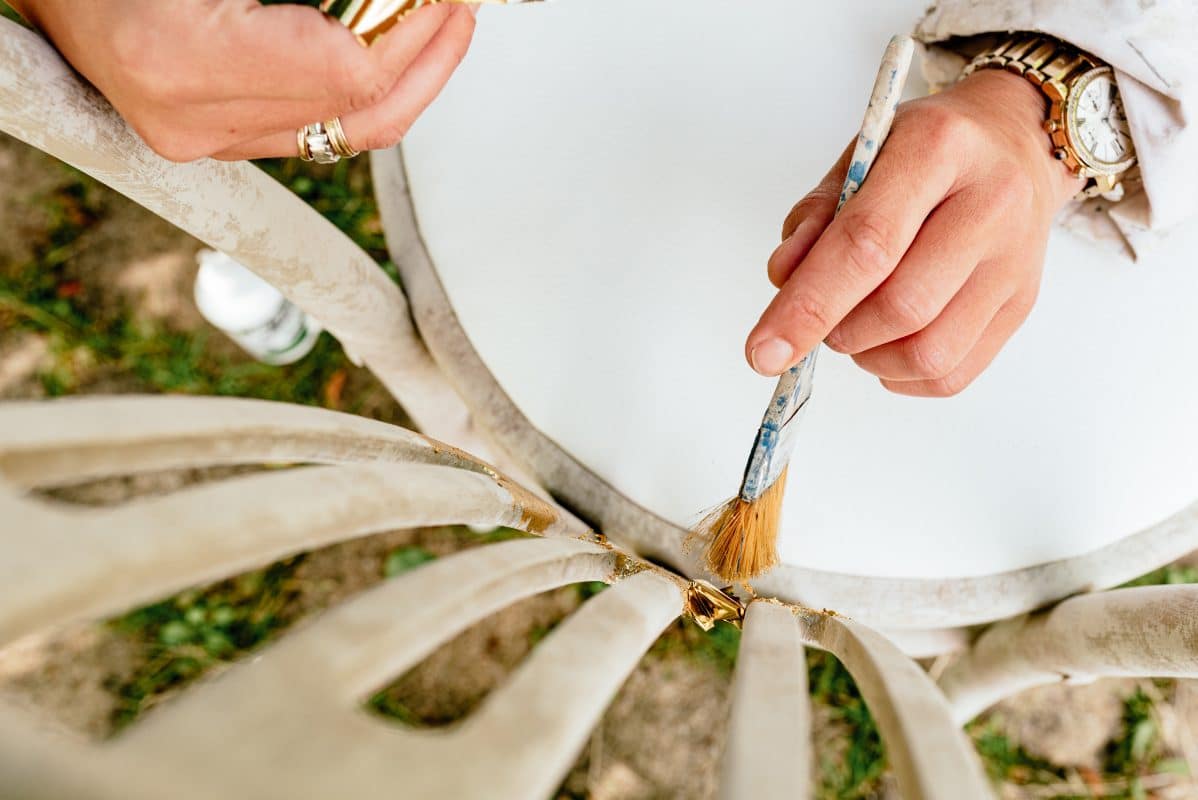 Hand streicht mit Pinsel weißen Stuhl an.