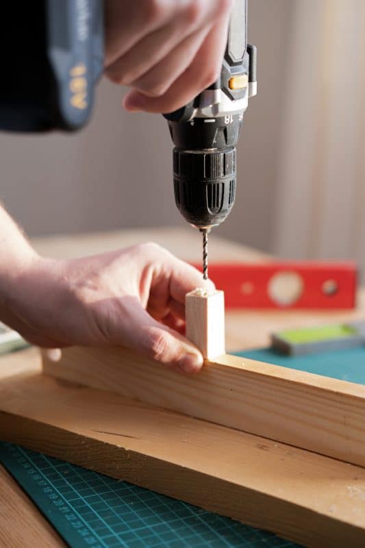 Bohrmaschine beim Bohren in ein kleines Holzstück auf Werkbank.