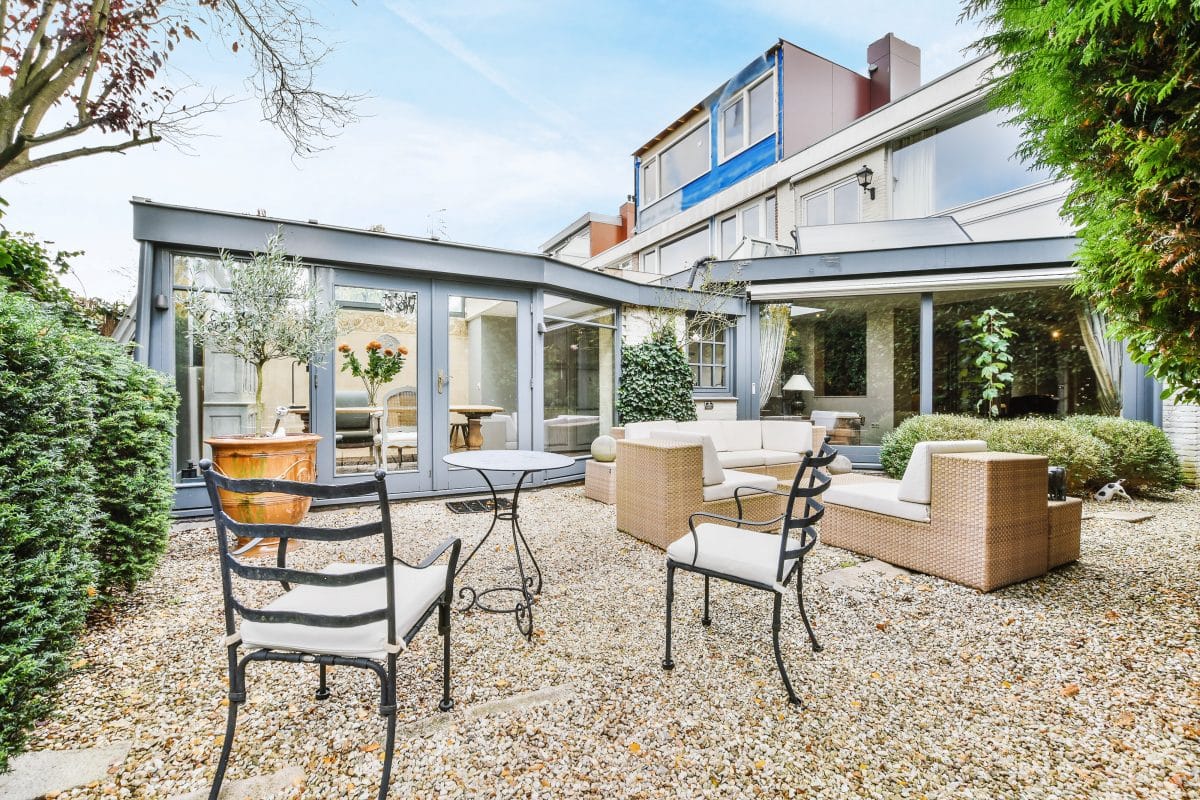 Großzügige Terrasse mit Rattanmöbeln und Kiesbelag im modernen Garten.