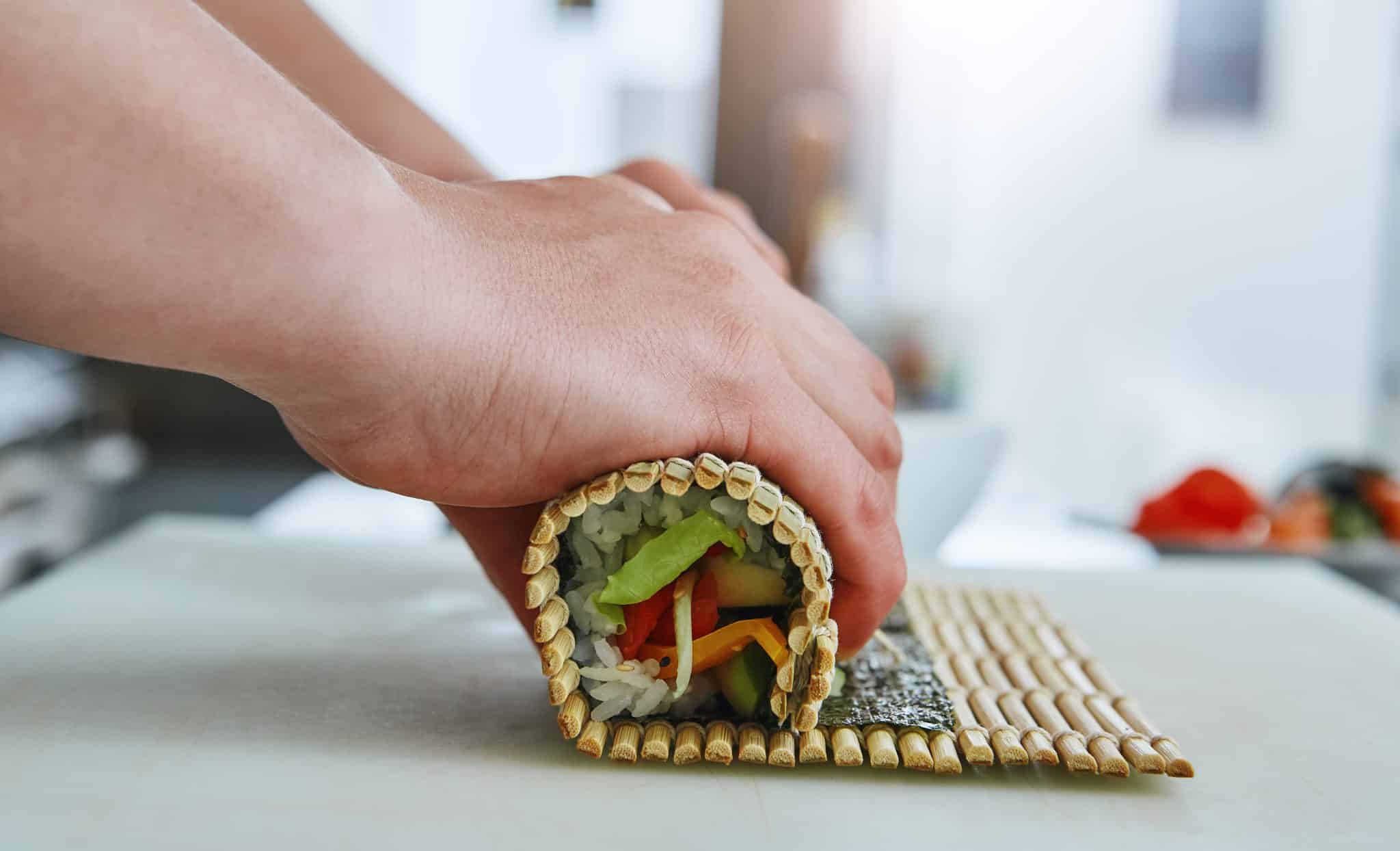 Sushirolle wird mit Bambusmatte sorgfältig geformt.