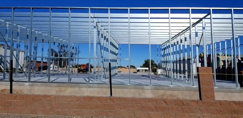 Stahlträger bilden eine offene Gebäudekonstruktion auf einem Betonfundament unter blauem Himmel.