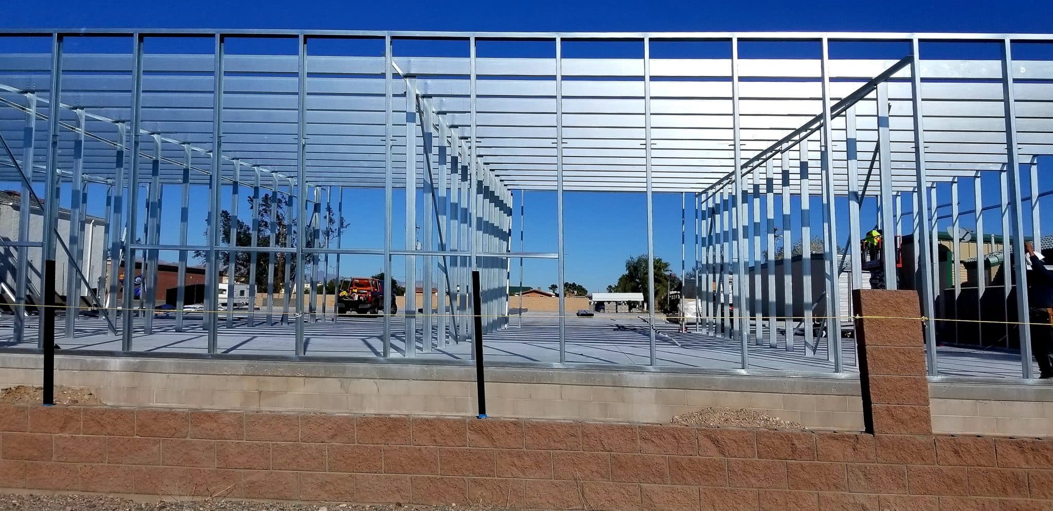 Stahlträger bilden eine offene Gebäudekonstruktion auf einem Betonfundament unter blauem Himmel.