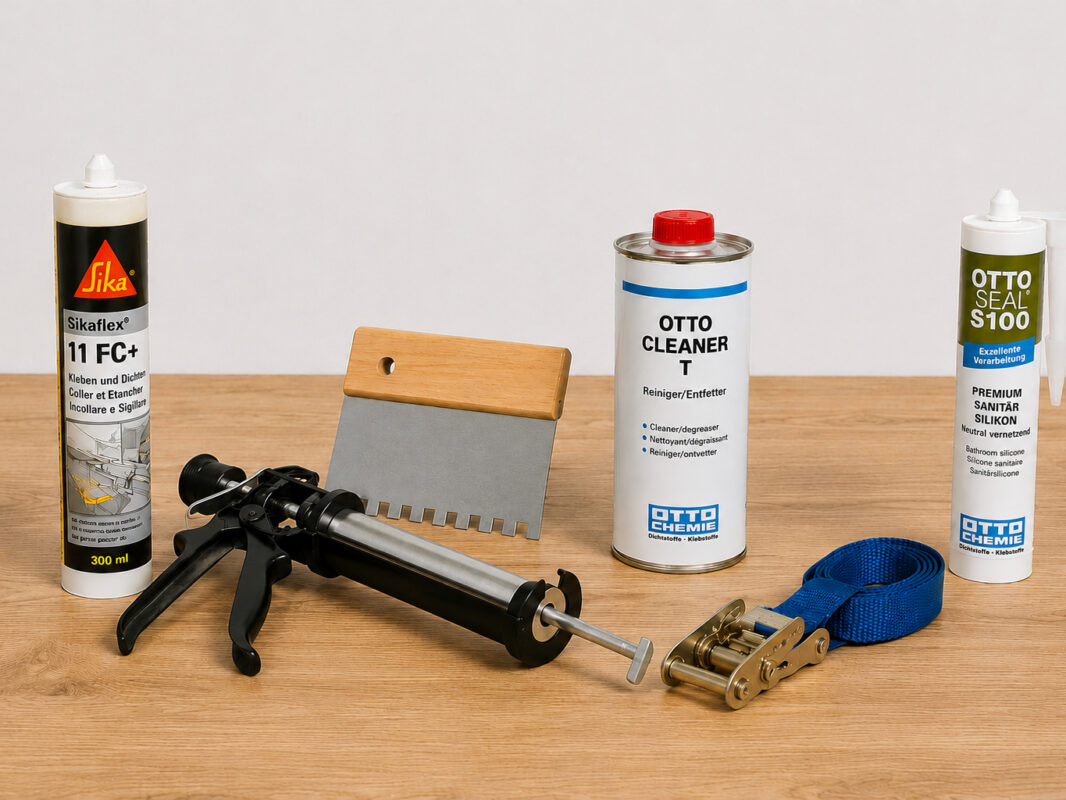 Montagematerial für Edelstahl-Arbeitsplatte mit Montagekleber, Kartuschenpistole, Kammspachtel, Reiniger, Silikon und Spanngurt übersichtlich angeordnet.