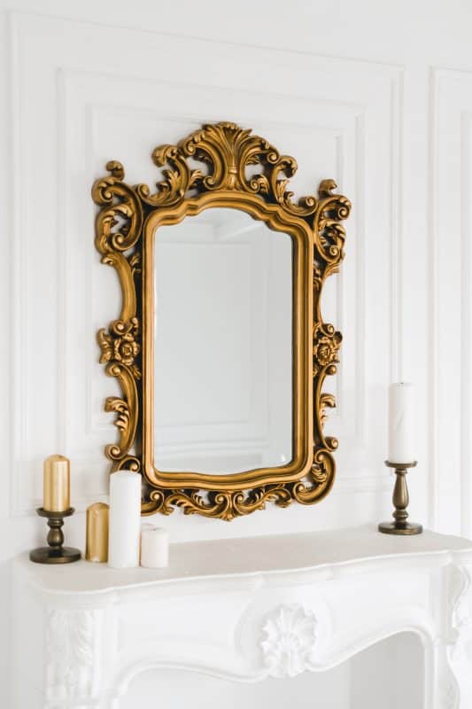 Goldener Barockspiegel über weißem Kamin mit Kerzen.