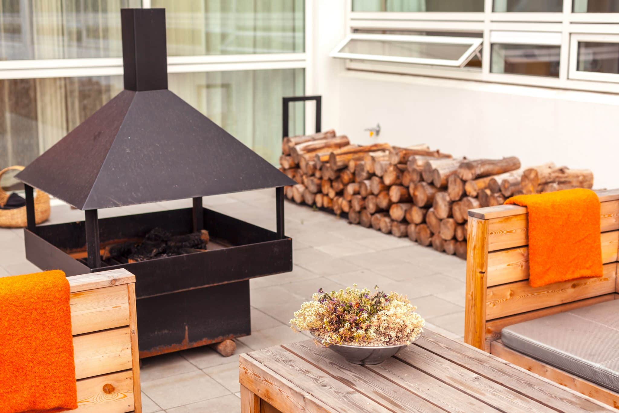 Gemütliche Terrasse mit Feuerstelle, Holzvorrat und Holzmöbeln.