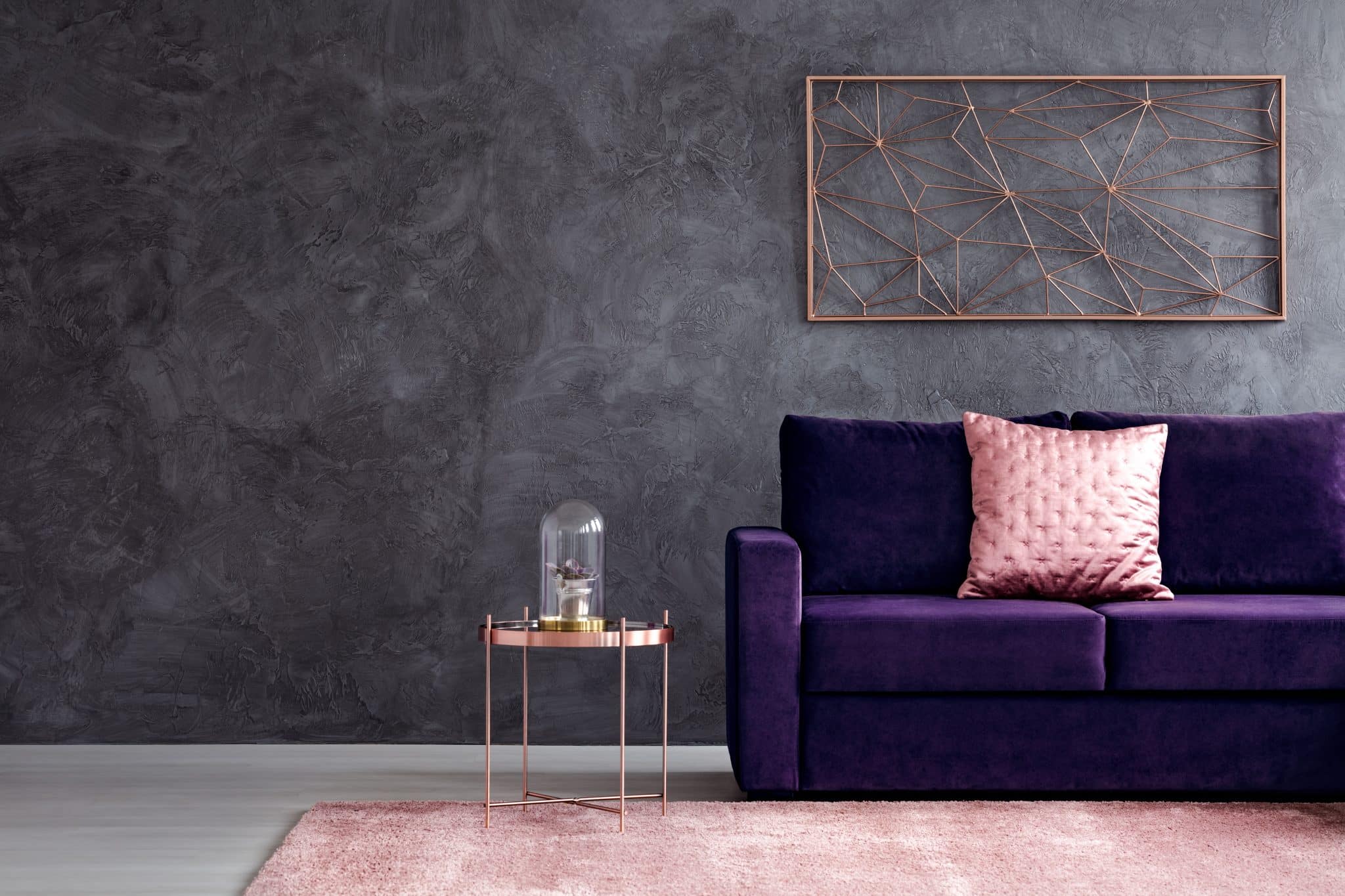 Ein violettes Sofa steht gemütlich vor einer dunkelgrauen strukturierten Wand.