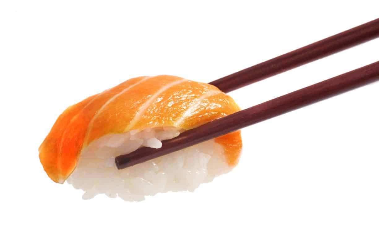 Lachs-Nigiri wird mit Essstäbchen gehalten.
