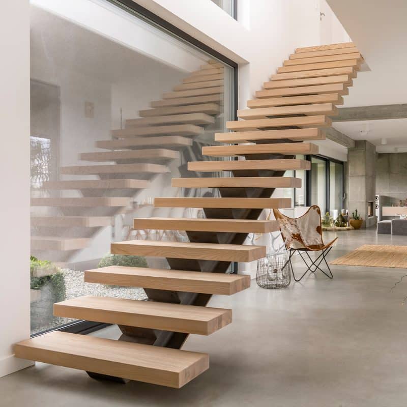 Eine moderne Holztreppe liegt zwischen weißen Wänden und führt zu einem Flur.