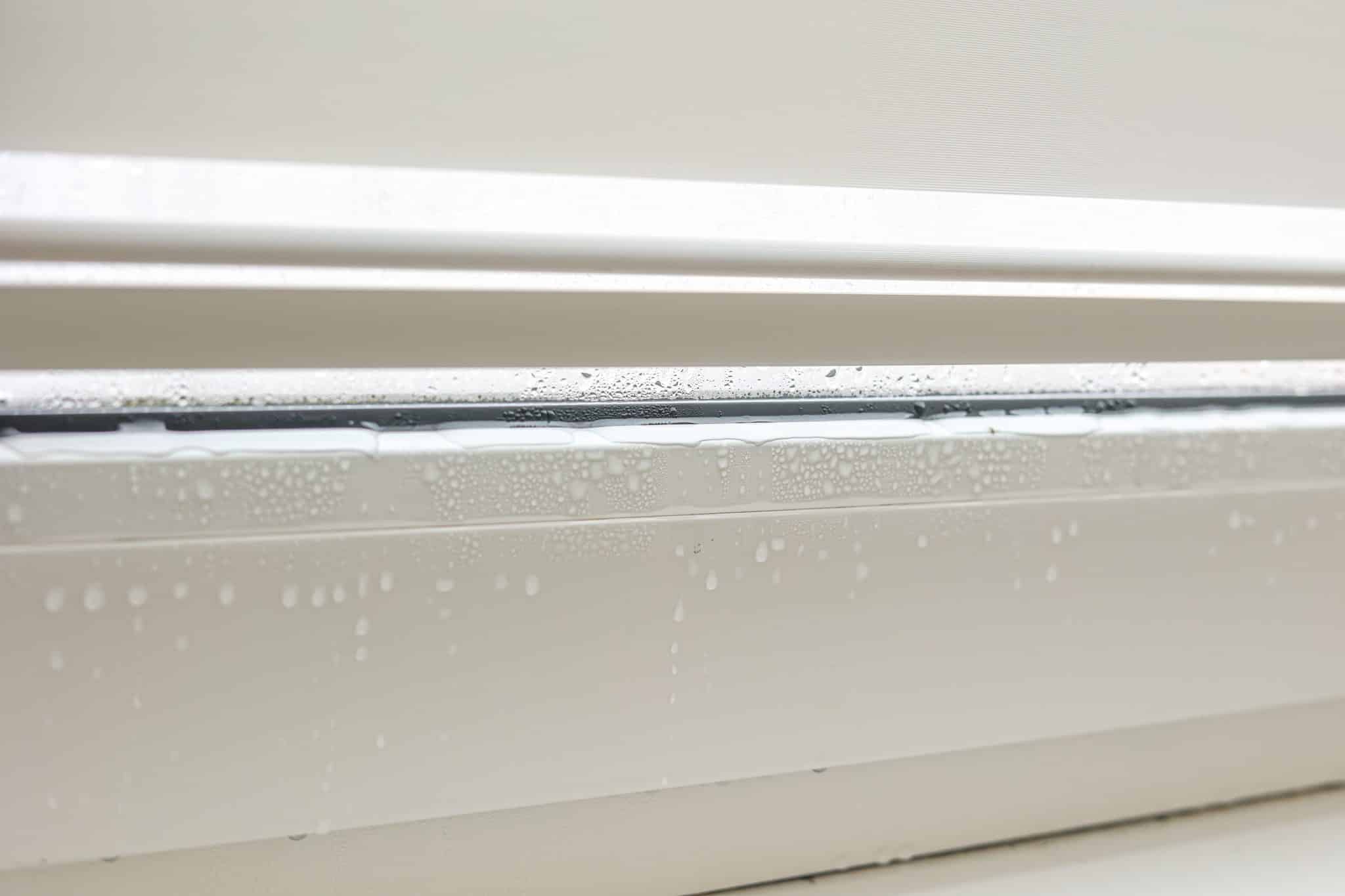 Wassertropfen sammeln sich auf einer weißen Fensterkante.