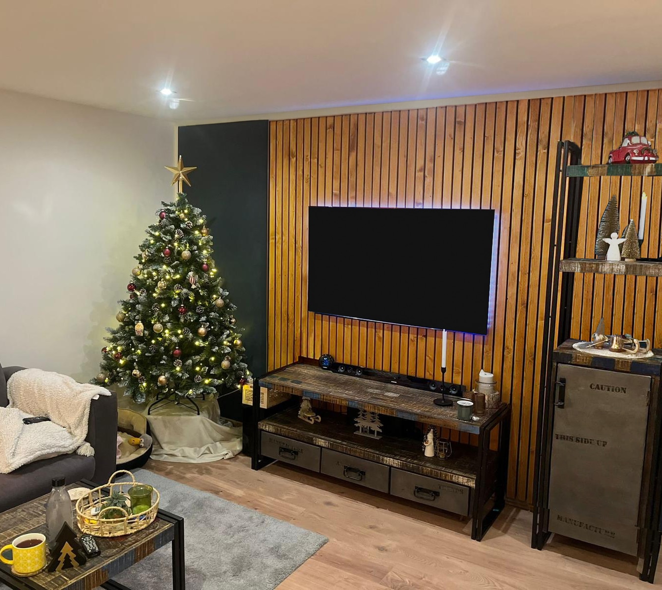Ein Wohnzimmer mit Weihnachtsbaum zeigt eine Holzwand und einen großen Fernseher.
