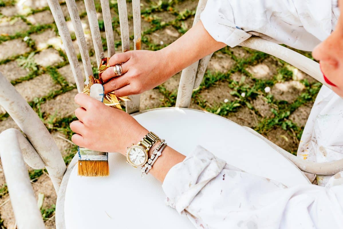 erson lackiert weißen Holzstuhl mit breitem Pinsel.