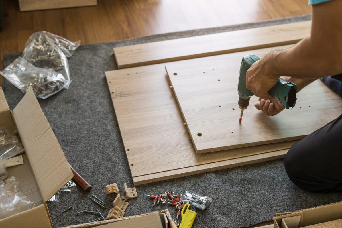 Möbelmontage mit Akkuschrauber und Holzteilen auf Teppich.
